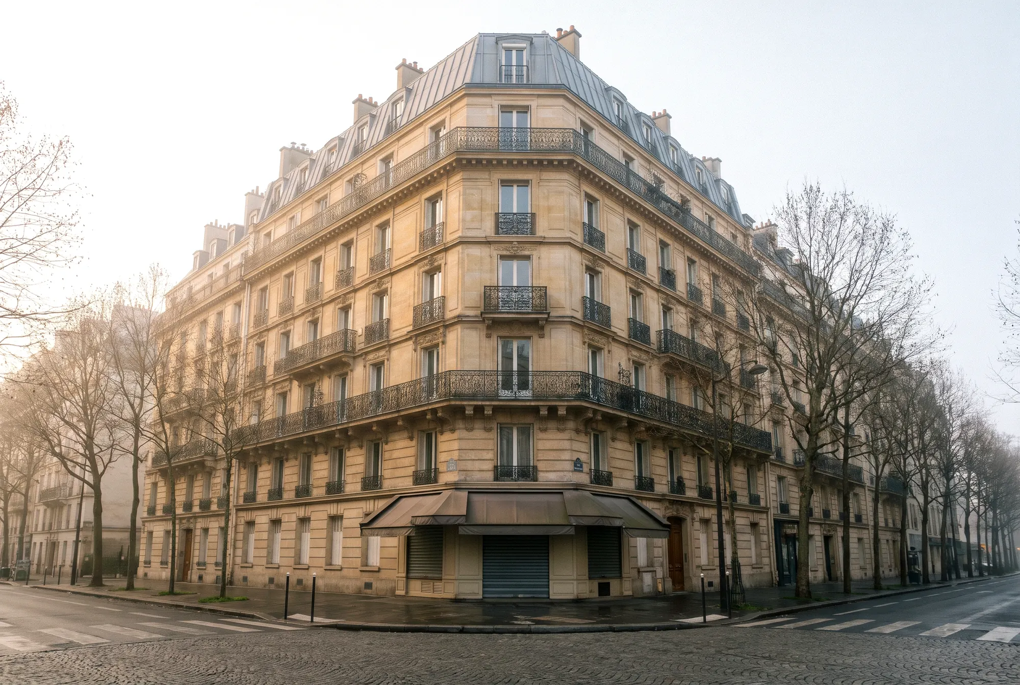 Façade haussmannienne en pierre de taille, balcons en fer forgé, rue arborée déserte au petit matin