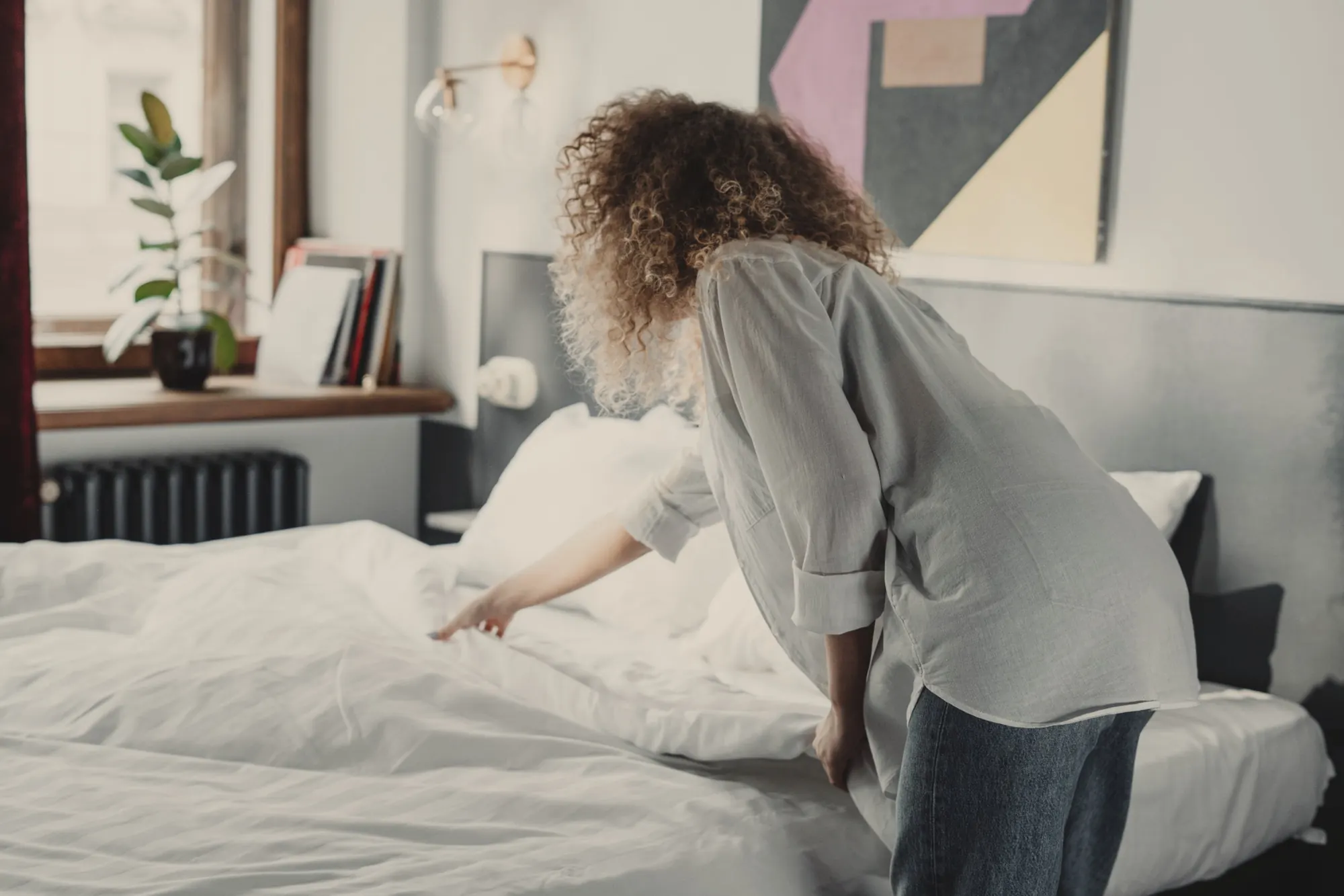 Intervenante qui tire la couette d’un lit blanc dans une chambre lumineuse