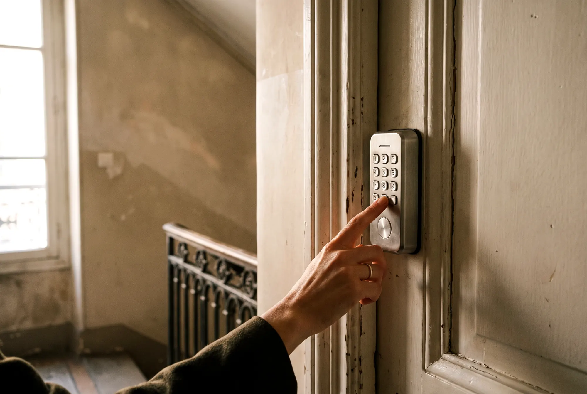 Une main compose le code d’une serrure connectée à clavier sur une porte d’appartement